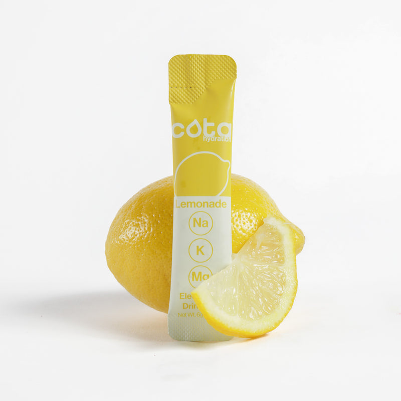 Cota Hydration lemonade electrolyte packet with a lemon and lemon slice on a white background
