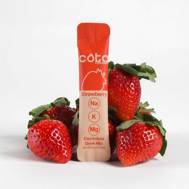 Cota Hydration strawberry electrolyte drink mix packet surrounded by strawberries on a white background