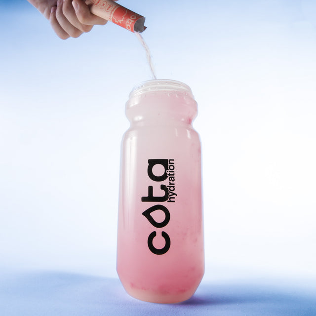 Cota Hydration water bottle being filled with a strawberry flavored Cota Hydration electrolyte packet on a light blue background