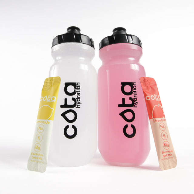 Two Cota Hydration water bottles, one white and one red, with two electrolyte drink mix packets on a white background.